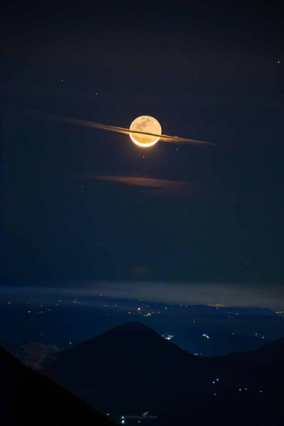 The featured image shows a crescent Moon over a city
and volcano with a flat cloud running through the center that
makes the Moon like a bit like the planet Saturn.
Please see the explanation for more detailed information.